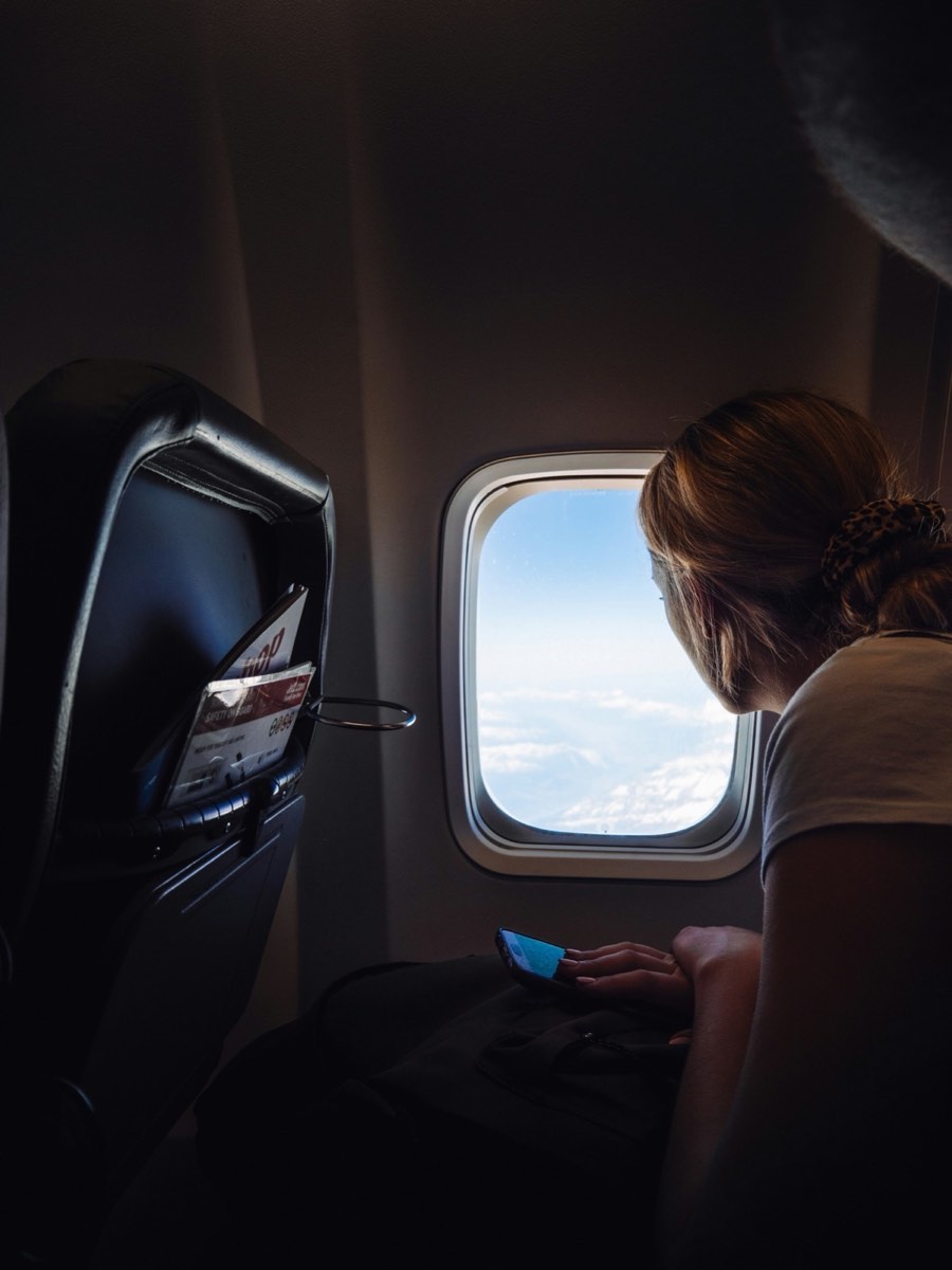 A young woman looking out an airplane window, representing the journey that a Wandering With Pride scholarship makes possible